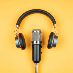 A studio microphone stands upright with large black headphones above it against a vibrant yellow background